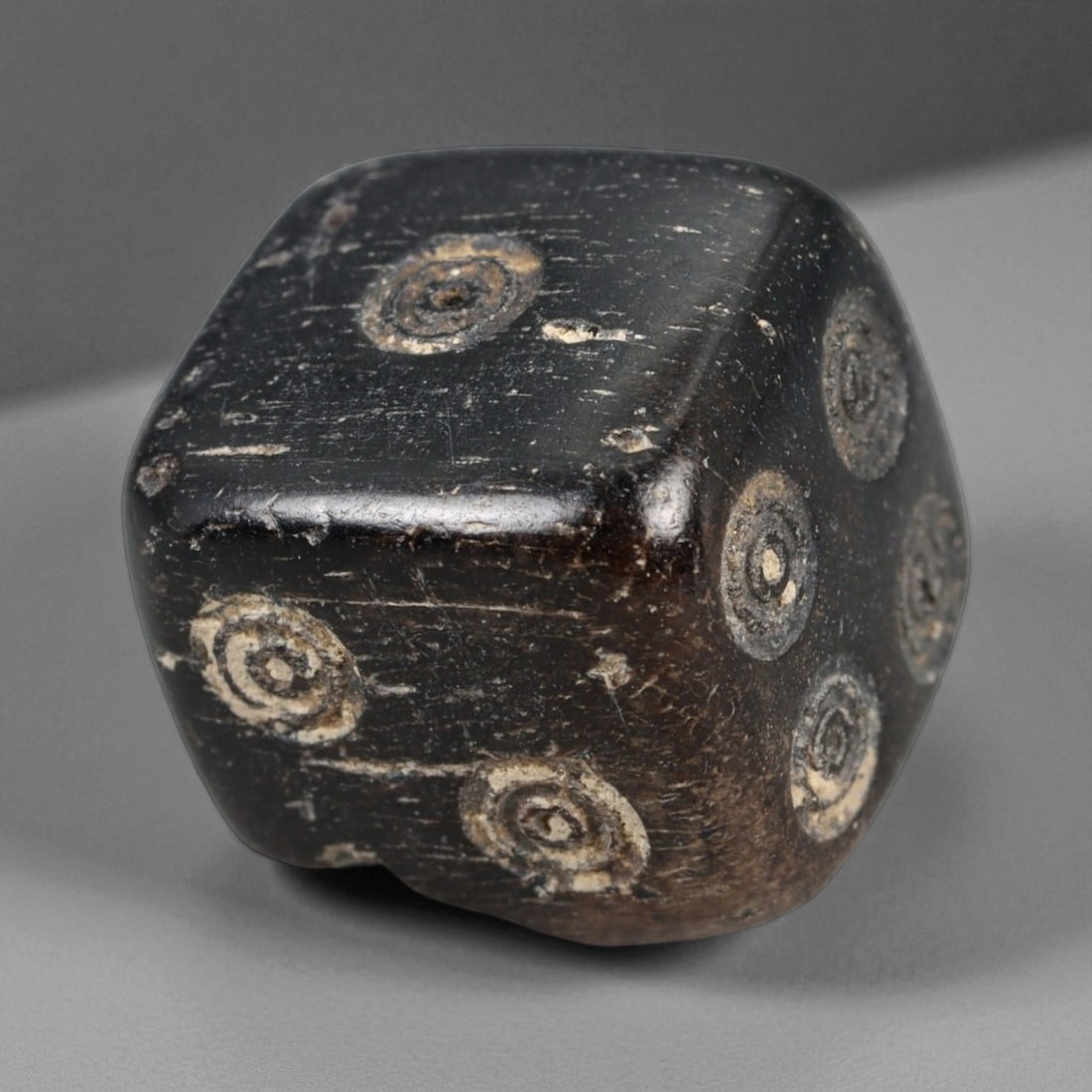 Ancient Roman Bone Dice with Ring-and-Dot Motifs, c. 1st-3rd Century CE, 1.3cm: This ancient Roman gaming die, carved from bone, dates to the 1st-3rd century CE, during the height of the Roman Empire. The cube is intricately engraved with the traditional ring-and-dot motifs used 