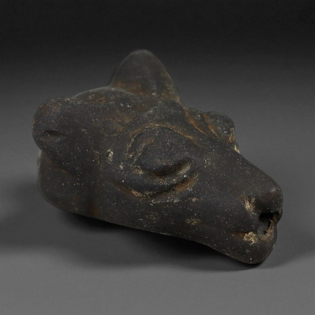 Ancient Levantine Panther Head Hematite Amulet, c. 15th-12th Century BCE 2.1cm: This compelling amulet, carved from dense black hematite, depicts the stylized head of a panther and dates to the Late Bronze Age Levant, circa 15th-12th century BCE. The feline form, with its sleek l