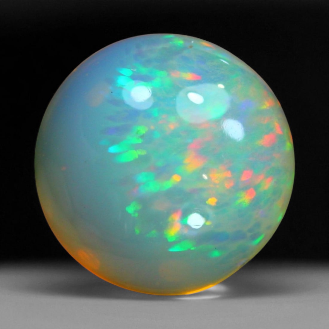 7.78 Carats Fiery Play-of-Color Welo Opal Oval Cabochon - Natural Ethiopian Stone: This mesmerizing Welo opal radiates a luminous play-of-color that dances across its translucent body in vivid flashes of red, orange, green, and violet 13.5x13.3x8.7mm. The gem's opalescent base glows