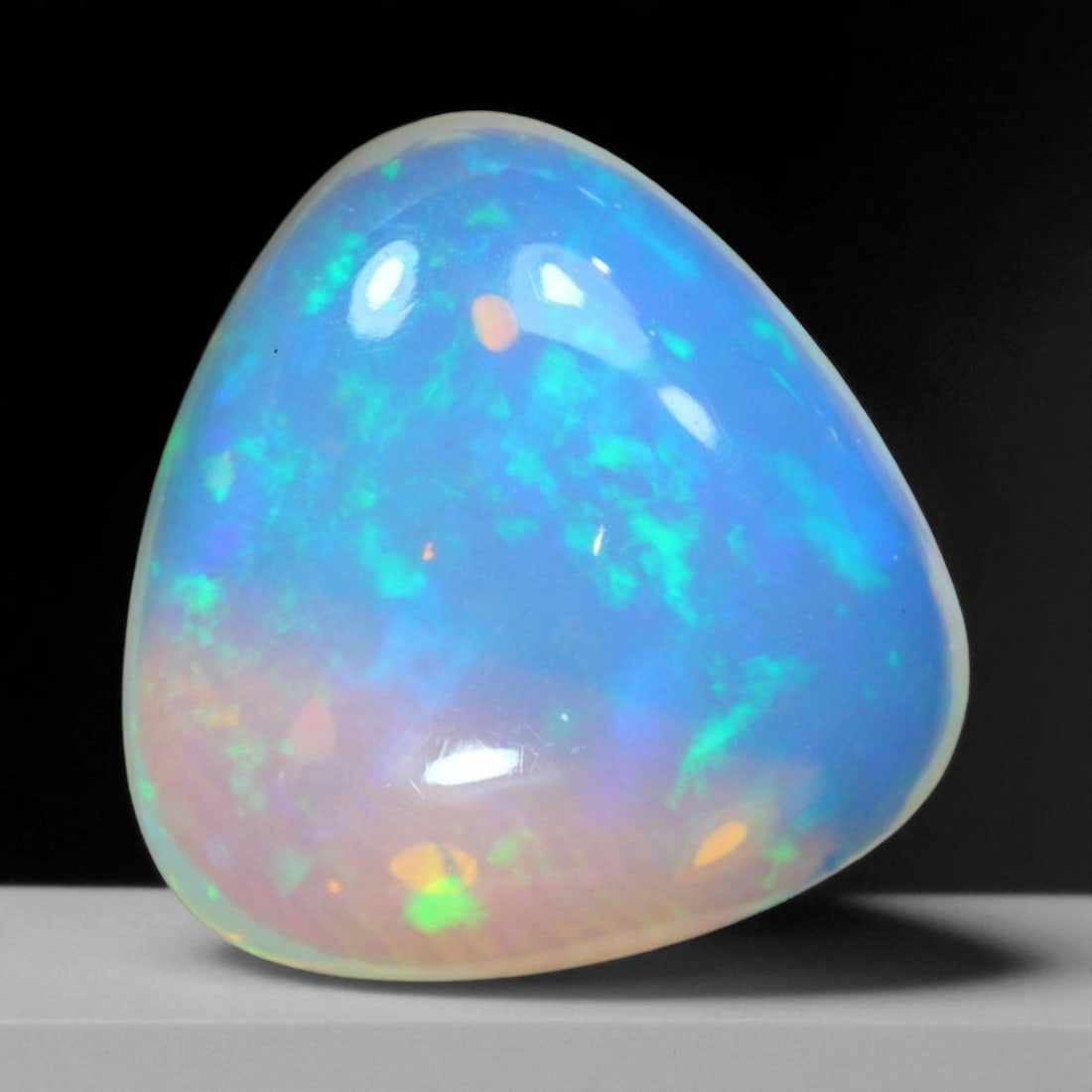 8.89 Carats Fiery Play-of-Color Welo Opal Oval Cabochon - Natural Ethiopian Stone: This mesmerizing Welo opal radiates a luminous play-of-color that dances across its translucent body in vivid flashes of red, orange, green, and violet 15.9x15.6x8mm. The gem's opalescent base glows w