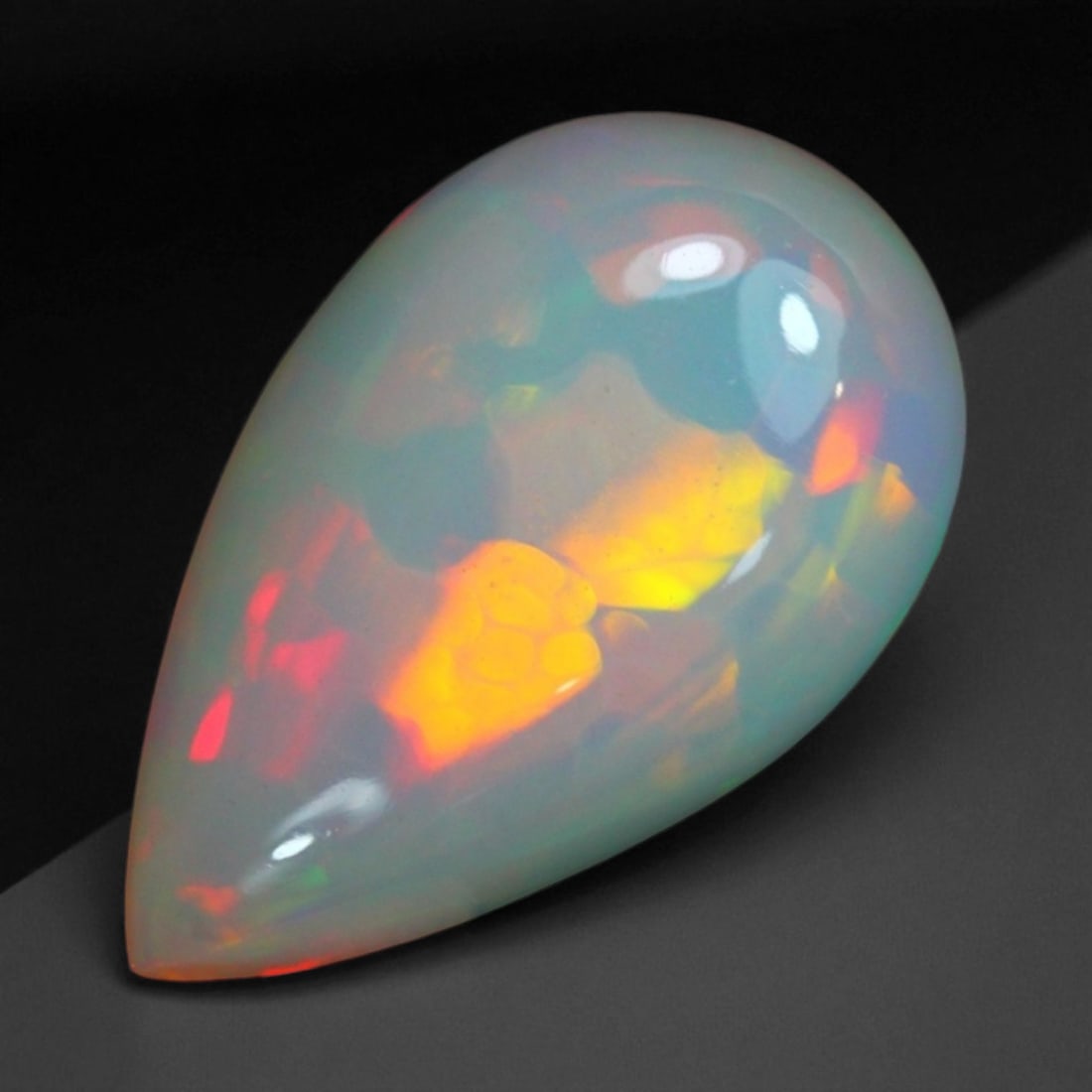 5.49 Carats Fiery Play-of-Color Welo Opal Oval Cabochon - Natural Ethiopian Stone: This mesmerizing Welo opal radiates a luminous play-of-color that dances across its translucent body in vivid flashes of red, orange, green, and violet 17.4x10.7x6.4mm. The gem's opalescent base glows