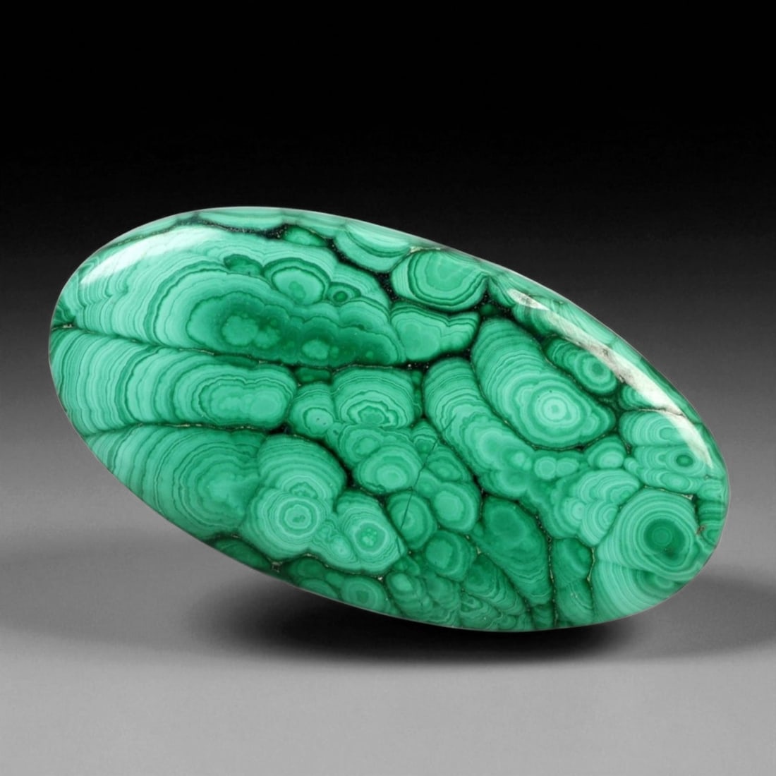 47.94 Carats Banded Forest Green Malachite Oval Cabochon - Natural Congolese Stone: This exceptional 47.94-carat malachite cabochon showcases mesmerizing concentric banding in vivid forest and mint green tones. The rhythmic circular patterns flow gracefully across its polished oval s