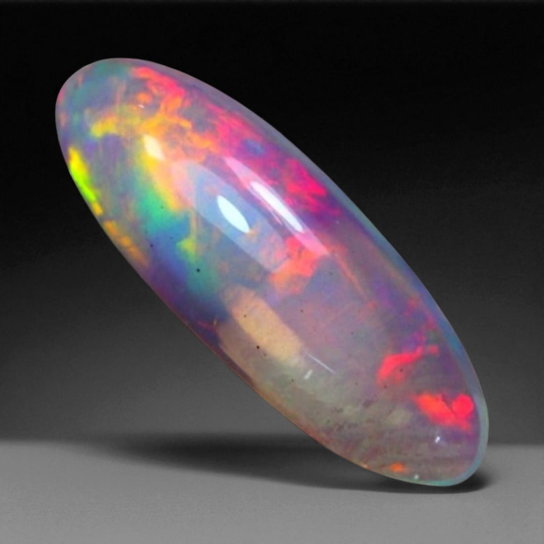 6.43 Carats Fiery Play-of-Color Welo Opal Oval Cabochon - Natural Ethiopian Stone: This mesmerizing Welo opal radiates a luminous play-of-color that dances across its translucent body in vivid flashes of red, orange, green, and violet 23x8.3x6.1mm. The gem's opalescent base glows wi