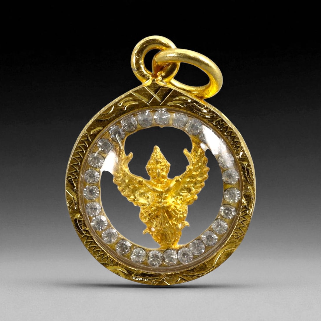Vintage Thai Garuda Emblem Amulet with Crystal Ring and Gilt Frame, c. Late 20th Century, 3g: This elegant and lightweight vintage Thai amulet features a gold-toned Garuda figure suspended mid-flight within a circular pendant framed by clear faux crystals. The amulet is set in a finely engrave