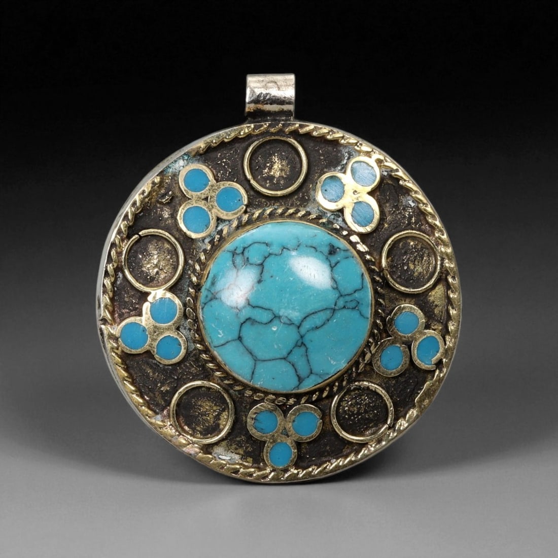 Vintage Himalayan Tribal Turquoise Brass Amulet Pendant, 20th Century, 4.5cm: This bold circular pendant exemplifies the spirit of Himalayan tribal craftsmanship, blending symbolic artistry with a rugged, time-honored aesthetic. At its center lies a vivid turquoise cabochon, na