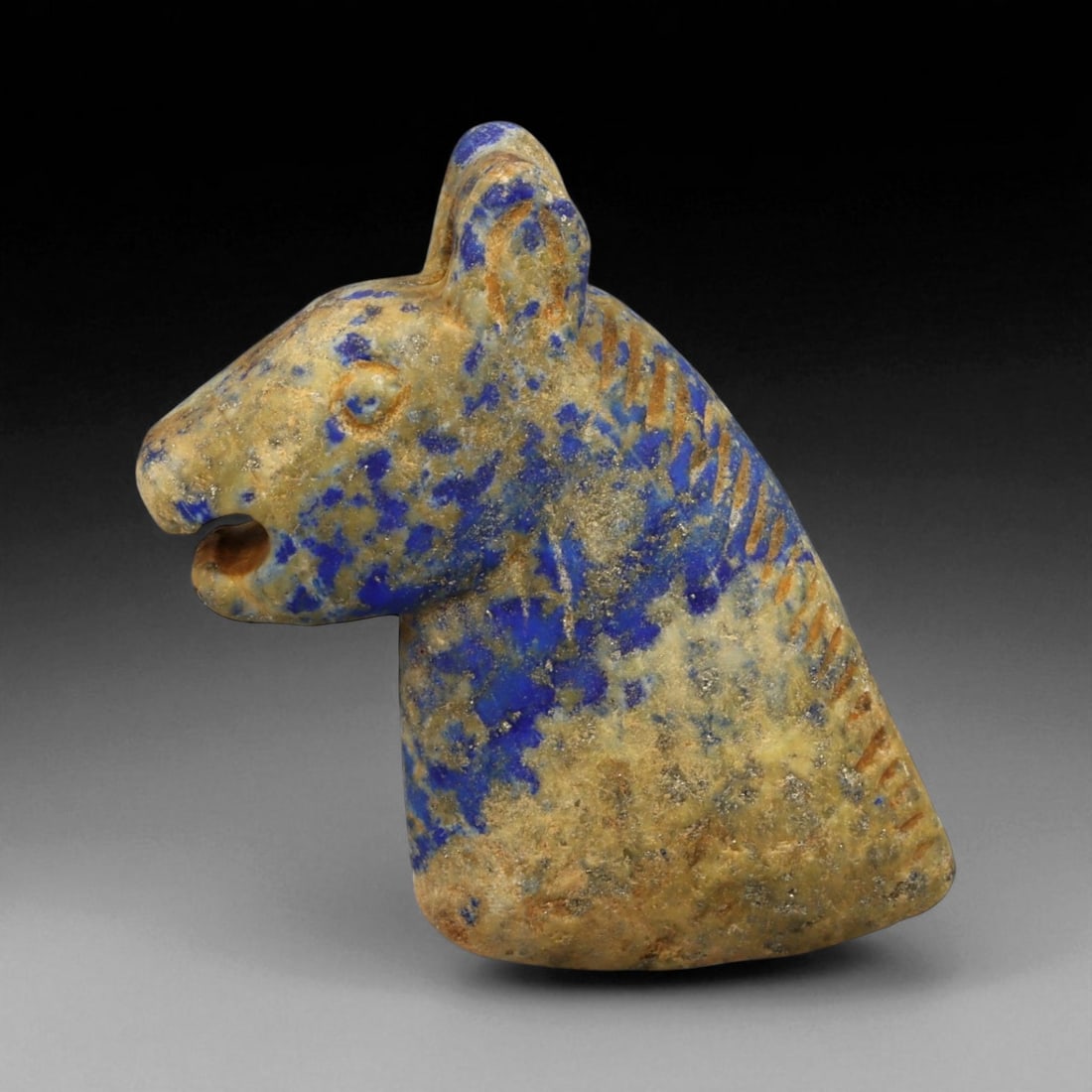 Ancient Bactrian Lapis Lazuli Horse Bust Amulet, c. 2nd-1st Millennium BCE, H 6.5cm: This remarkable horse bust amulet, carved from vivid lapis lazuli, originates from ancient Bactria, circa 2nd-1st millennium BCE. The sculpture embodies the region's distinctive blend of stylized eleg