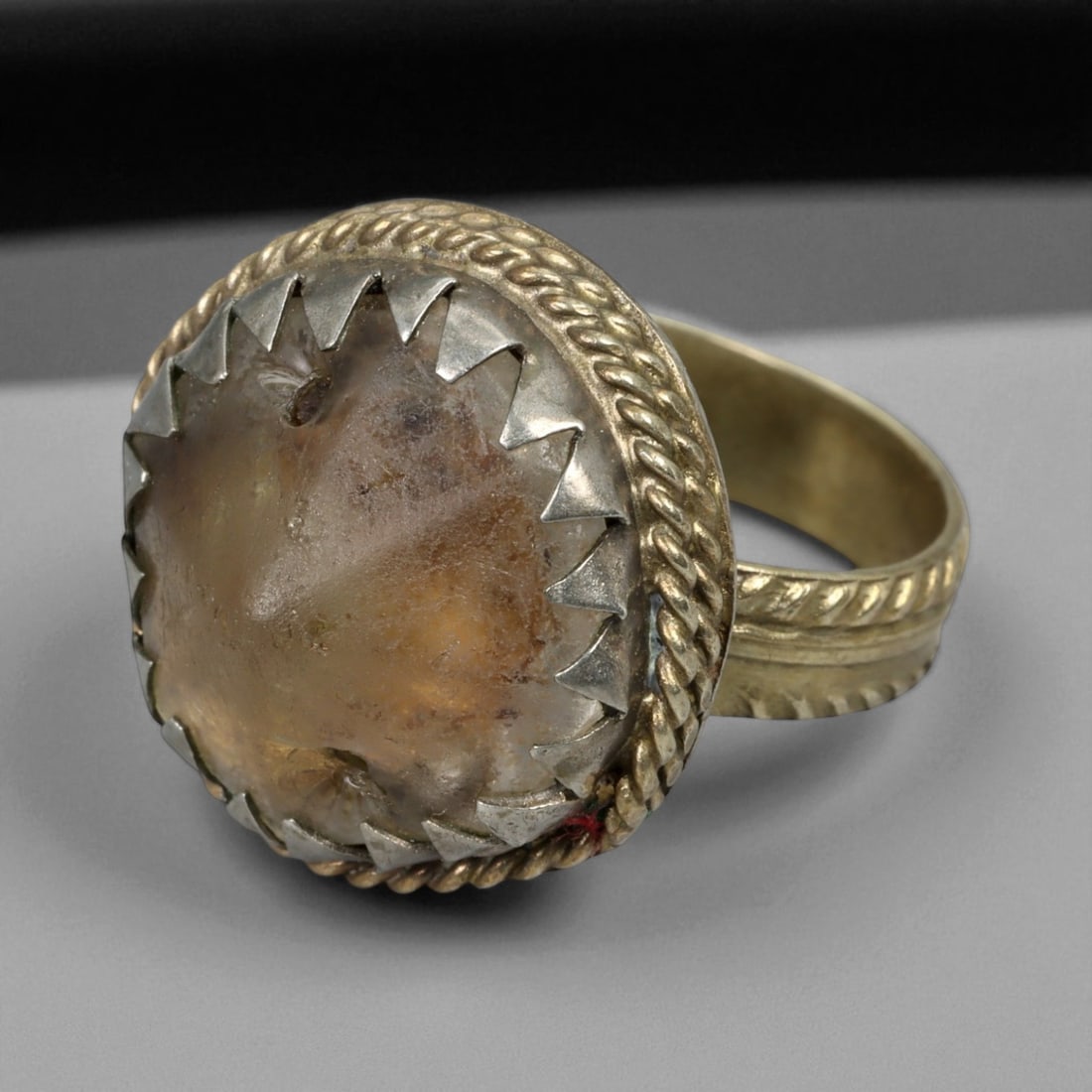 Antique Central Asian Silver Ring with Quartz Cabochon, c. 19th-20th Century, 8g: This antique silver ring reflects the enduring talismanic traditions of Central Asian jewelry. The bezel is set with a domed quartz cabochon, secured in a jagged toothed setting framed by twisted silv