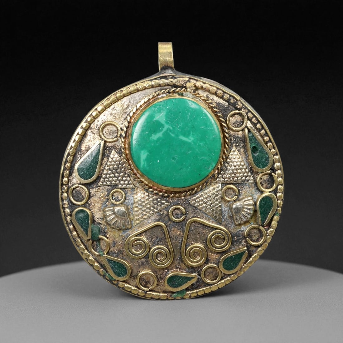 Vintage Himalayan Tribal Green Stone Brass Ritual Pendant, 20th Century, 5cm: This captivating circular pendant embodies the vibrant artistry of 20th-century Himalayan tribal craftsmanship, merging sacred geometry and symbolic design with traditional metalwork. At its heart lie