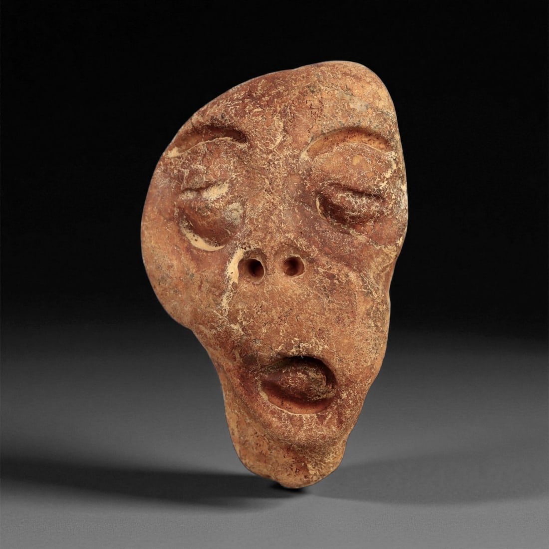 Ancient Medieval Levantine Stone Maskette Idol, c. 9th-12th Century CE, 4.5cm: This haunting stone maskette originates from the Medieval Levant, a crossroads of Byzantine and early Islamic cultural traditions. Carved from reddish-brown stone, the piece portrays a deeply expressi