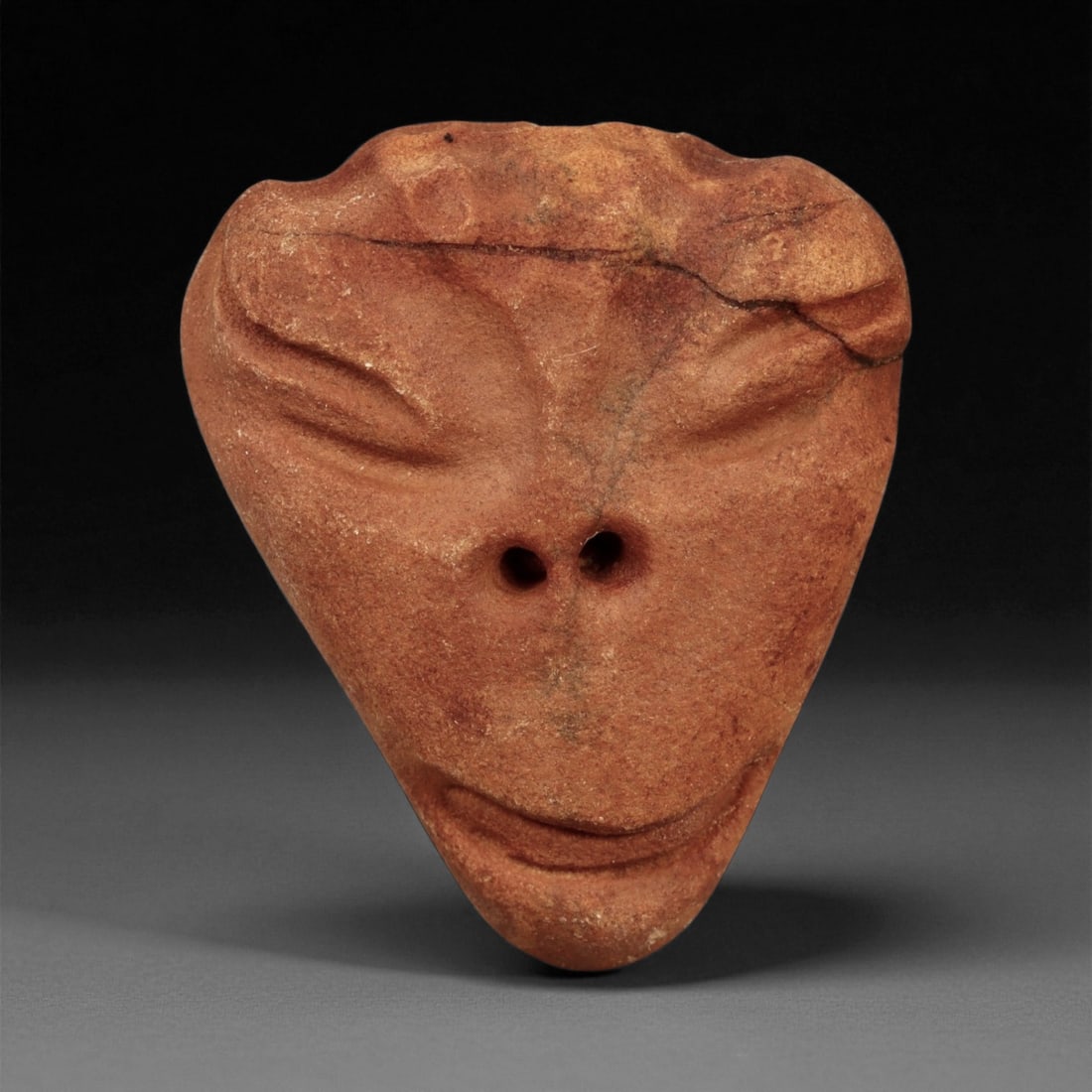 Ancient Medieval Coptic Egyptian Stone Maskette Amulet, c. 6th-9th Century CE, 4cm: This serene and stylized stone maskette originates from the Coptic period of early Christian Egypt, dating approximately between the 6th and 9th centuries CE. Carved from fine-grained reddish stone, t