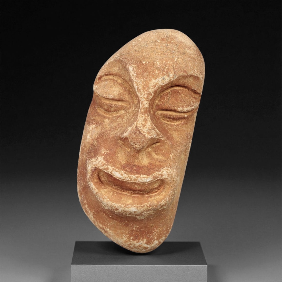 Ancient Medieval African Stone Maskette Amulet, c. 15th-17th Century CE, 4.5cm: This striking stone maskette amulet, carved from warm reddish-brown stone, represents the deeply spiritual artistry of African folk carving during the late medieval to early modern period. The oval fa