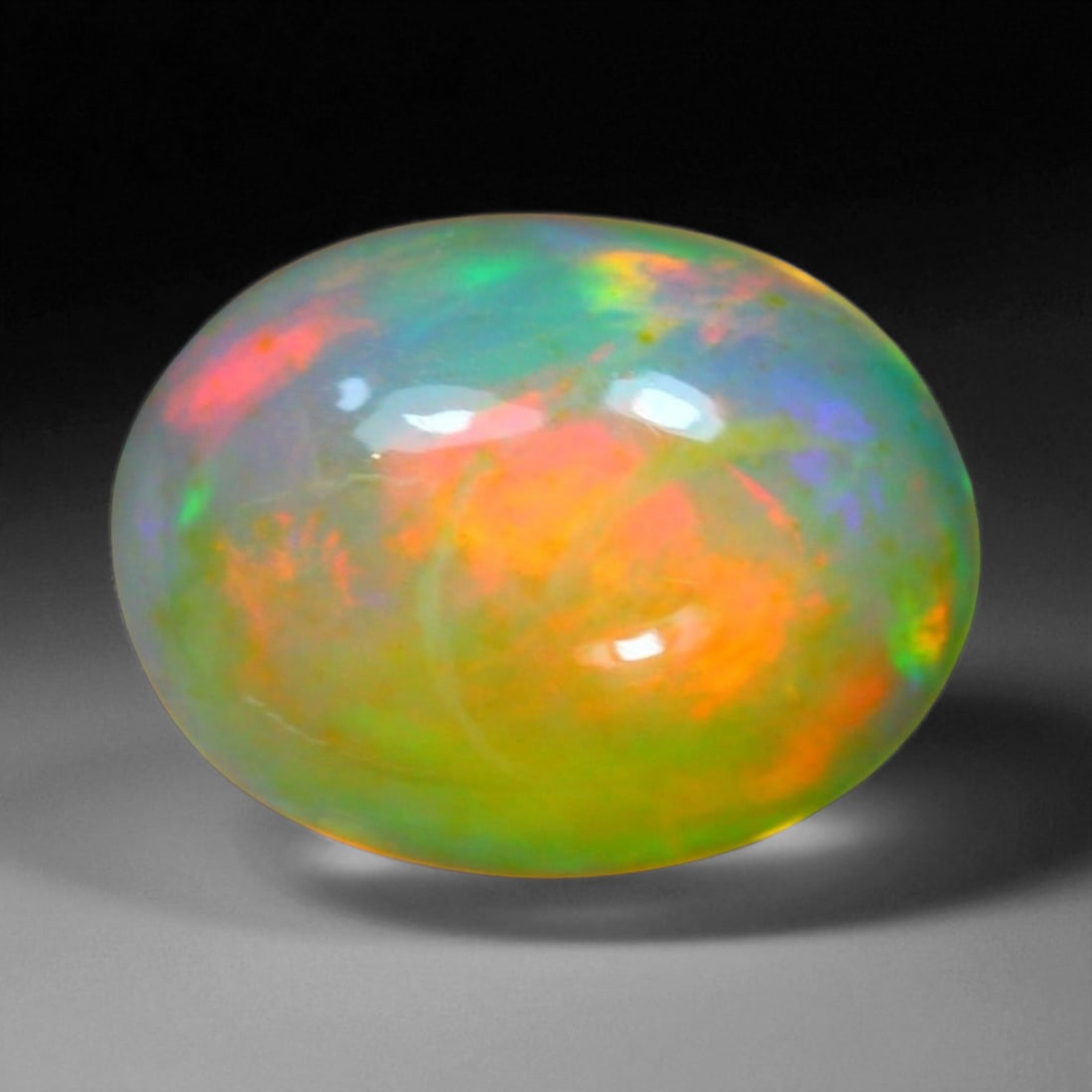 4.10 Carats Fiery Play-of-Color Welo Opal Oval Cabochon - Natural Ethiopian Stone: This mesmerizing Welo opal radiates a luminous play-of-color that dances across its translucent body in vivid flashes of red, orange, green, and violet 13.0x10.0x6.1mm. The gem's opalescent base glows