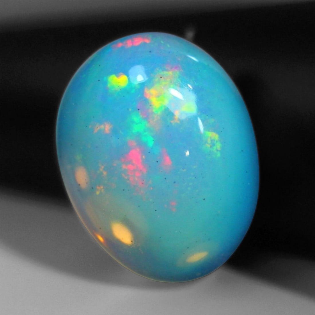 6.62 Carats Fiery Play-of-Color Welo Opal Oval Cabochon - Natural Ethiopian Stone: This mesmerizing Welo opal radiates a luminous play-of-color that dances across its translucent body in vivid flashes of red, orange, green, and violet 15.1x11.8x6.9mm. The gem's opalescent base glows