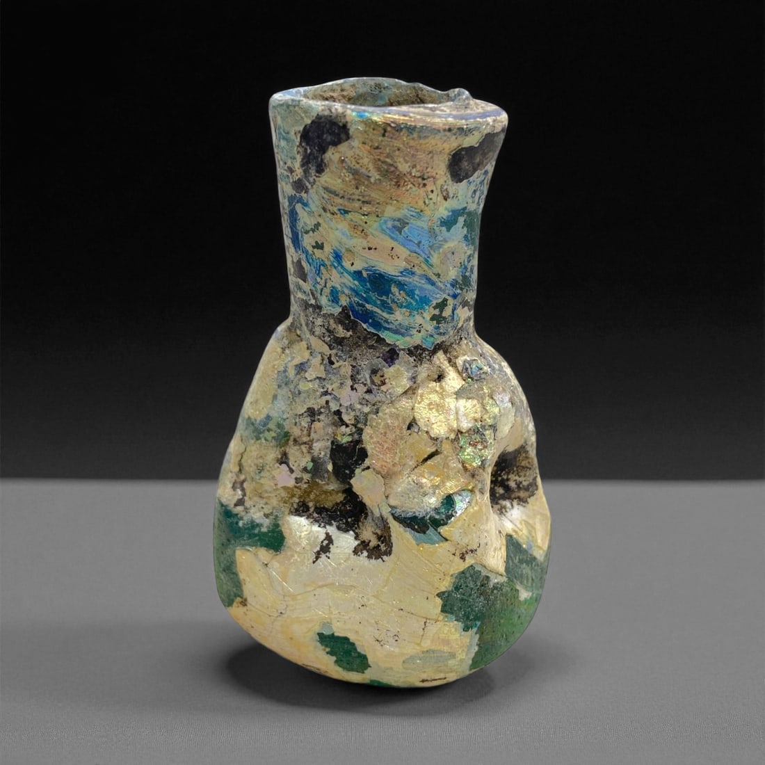 Ancient Roman Iridescent Glass Unguentarium, c. 1st-3rd Century CE, 6.5cm, 74g: This exquisite Roman glass unguentarium, dating to the 1st-3rd century CE, captures the poetic beauty and technical mastery of Roman glassmakers. Crafted in translucent glass now richly weathered with