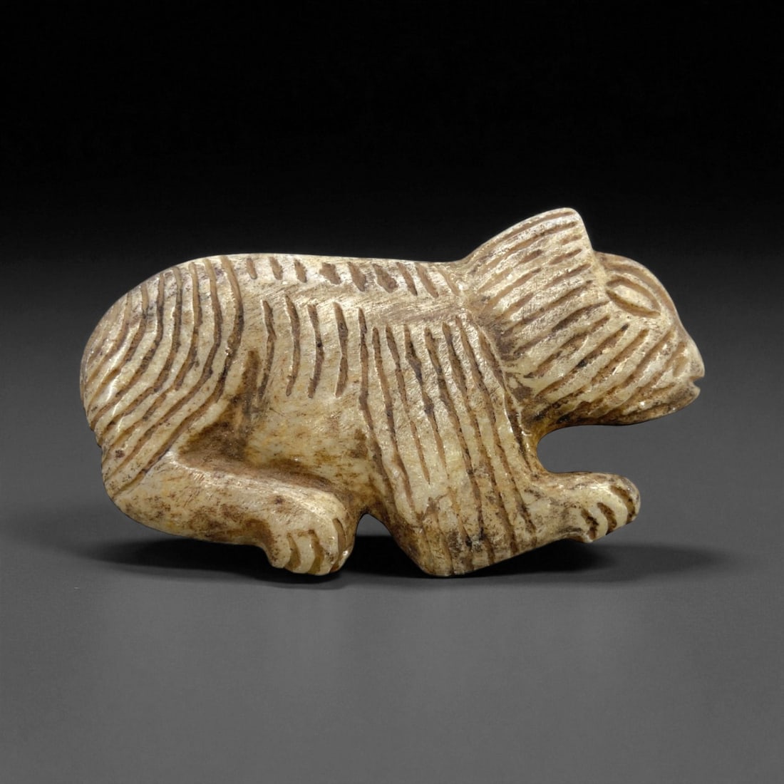Ancient Mesopotamian Striated Feline Effigy Amulet, c. 3rd-2nd Millennium BCE, 9cm, 103g: This remarkable feline effigy amulet, carved from a dense cream-colored stone and etched with deep striations, originates from ancient Mesopotamia and dates to the 3rd-2nd millennium BCE. Its stylized