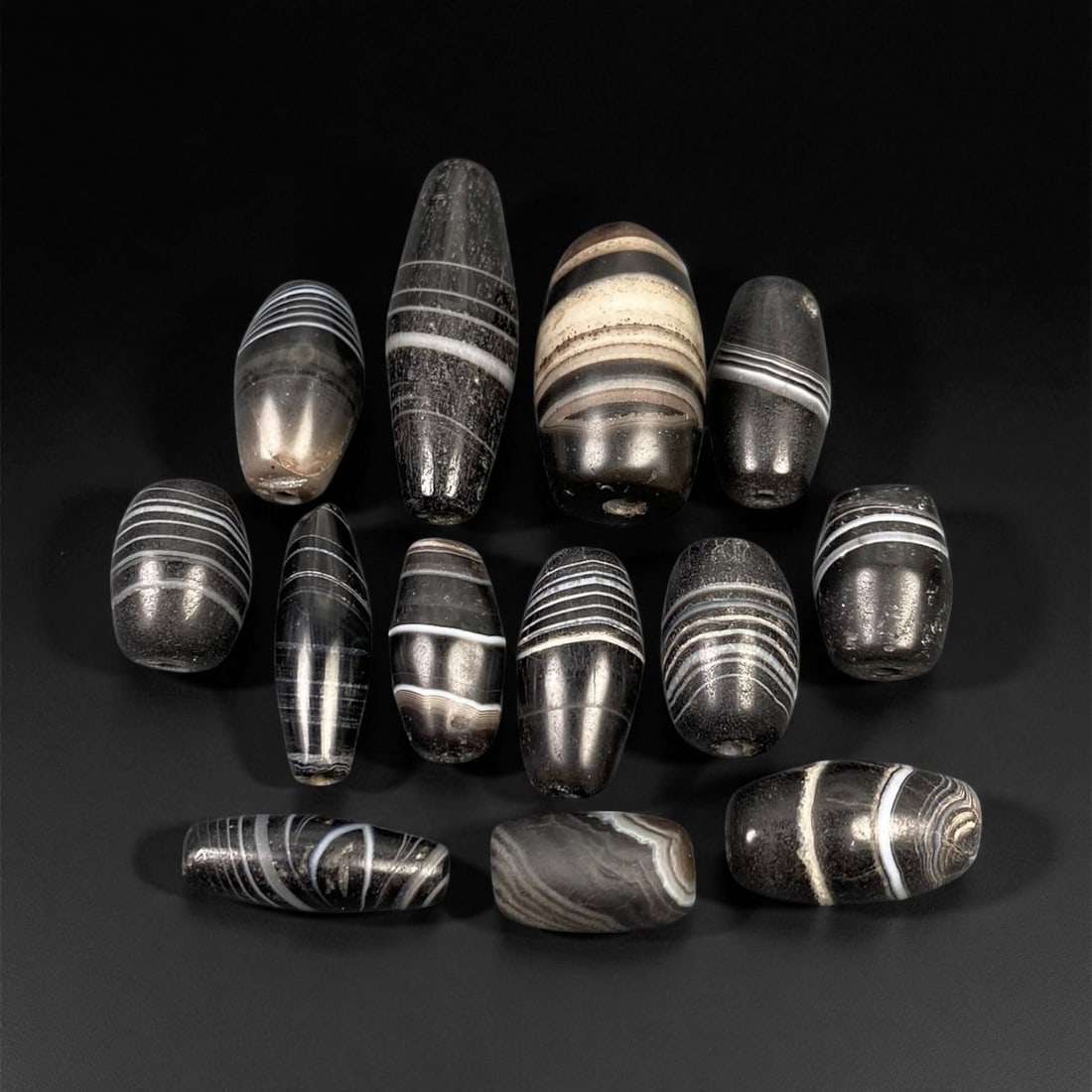 Ancient Bactrian Banded Agate Barrel and Ovoid Beads, c. 2nd Millennium BCE, 1.4-3cm: This remarkable assemblage of thirteen ancient banded agate beads originates from the Bactrian region of Central Asia, dating to the 2nd millennium BCE. Each bead is masterfully shaped into barrel and