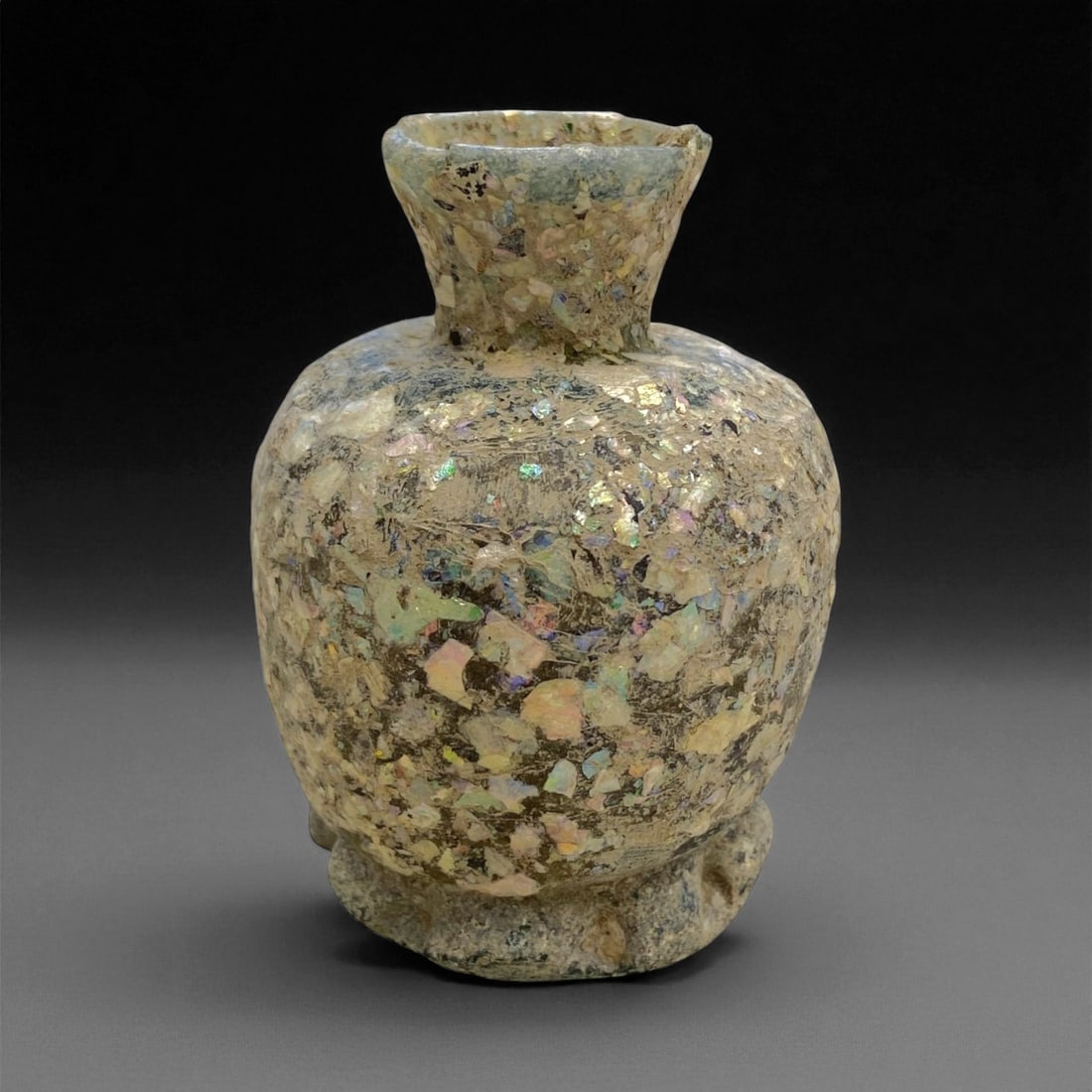 Ancient Roman Iridescent Glass Jar, c. 1st-3rd Century CE, 7cm, 96g: This impressive Roman glass jar, dating from the 1st-3rd century CE, is a magnificent example of early Imperial glass artistry. Blown from translucent glass that has since weathered into a radiant spe