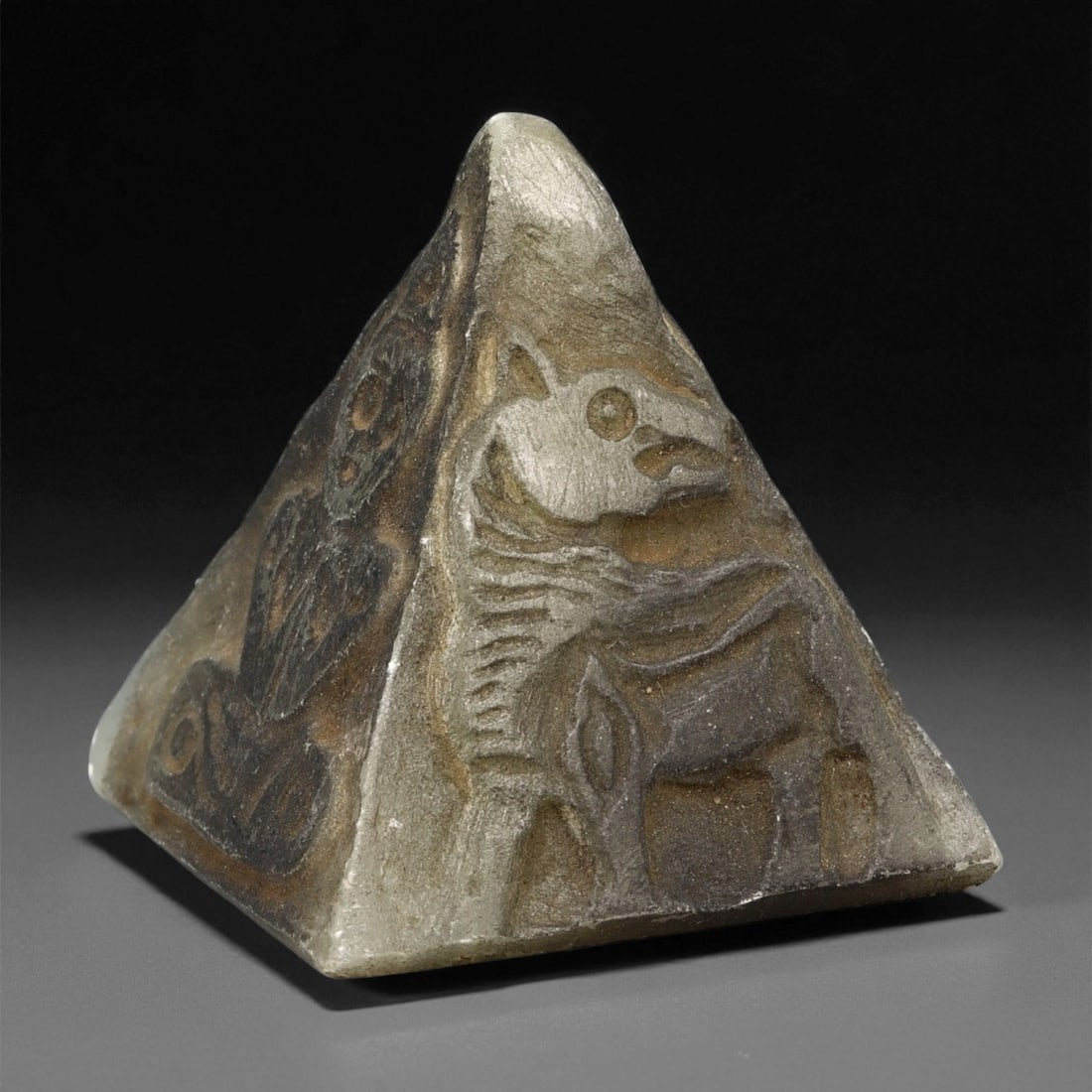 Ancient Mesopotamian Steatite Pyramid with Divine Reliefs, c. 2nd-1st Millennium BCE, 5.7cm: Carved from fine dark-grey steatite and polished to a soft sheen, this pyramidal votive object stands 5.7 cm tall and features reliefs on each of its four faces. Each side bears a distinct depiction f