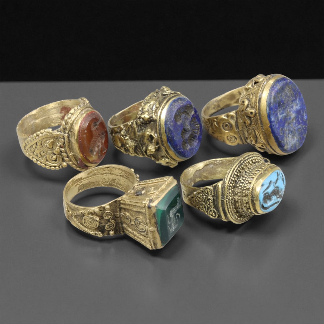 Antique Qajar Royal Gemstone Gilt Brass Rings Set, c. 18th-19th Century,: This refined set of five antique gilt brass rings originates from the Qajar Dynasty of Persia, dating to the 18th-19th century. Each ring is crafted with exquisite ornamental detailing and inset with