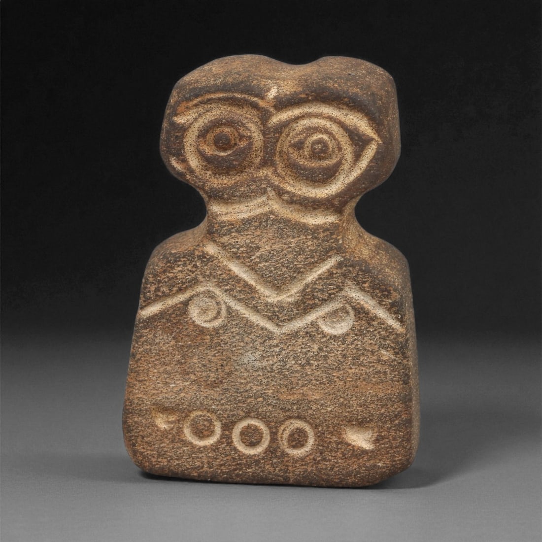 A Near Eastern Stone Eye Idol, 4th-3rd Millennium BCE, 2ZA: Carved from a brown stone with lighter surface veining, the figure is shaped with a rounded head bearing two recessed circular eyes formed by concentric grooves, the right eye showing a more angular e