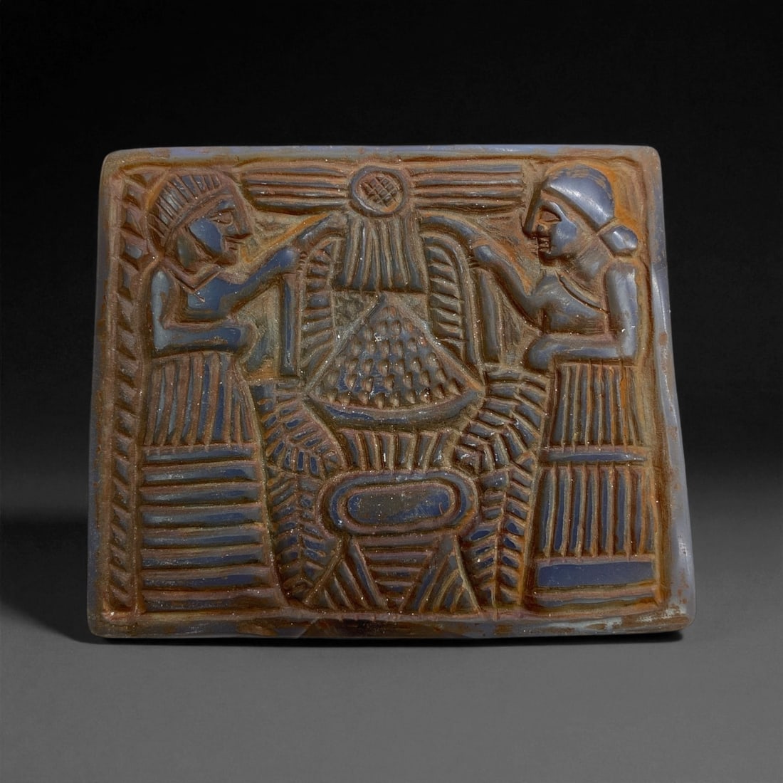 A Near Eastern Chalcedony Plaque Relief, Early Islamic Period, 8th-12th Century CE, 432g, 4EE: Carved from banded chalcedony with dark blue and brown tonal variations, the rectangular plaque bears a low-relief composition arranged in a single register. Two facing figures stand to either side of