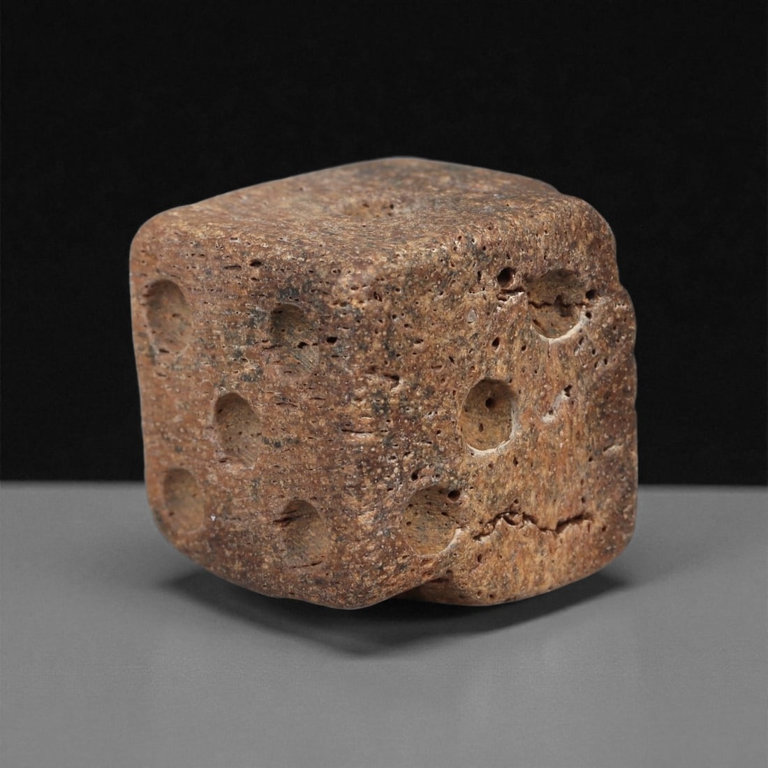 A Roman Bone Die, 1st-3rd Century CE, 43ZA: Carved from dense bone, the object is shaped as a small cube with slightly rounded edges. Each face bears a series of drilled circular pips arranged in standard numerical configurations. The surfaces 