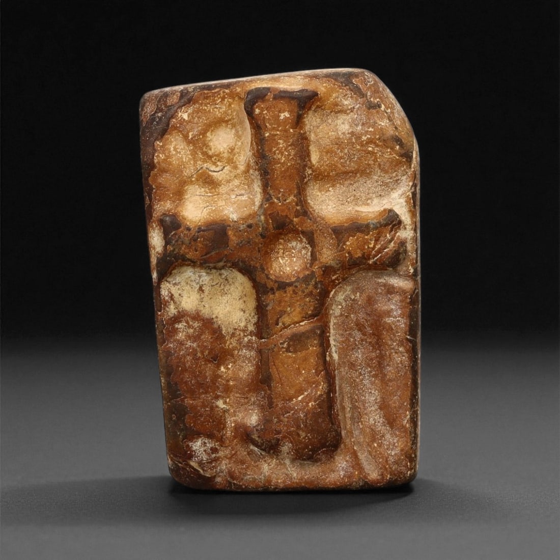 A Byzantine Stone Plaque with Incised Cross, 5th-7th Century CE, 26LA: Carved from brown stone with lighter surface encrustations, the plaque is rectangular with a slightly oblique upper corner. The front bears a cross rendered in low relief, formed by broad recessed arm