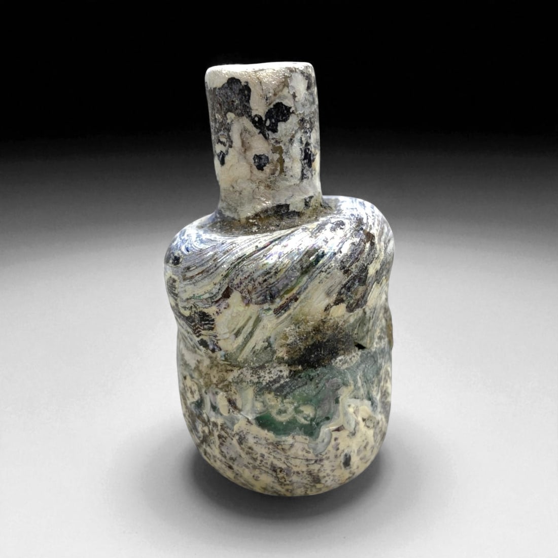 Ancient Roman Iridescent Glass Unguentarium, c. 1st-3rd Century CE, 6cm, 49g, 24AA: This delicate ancient Roman glass unguentarium, dating to approximately the 1st-3rd century CE, exemplifies the refined artistry and technical mastery of Roman glassmakers at the height of their craft