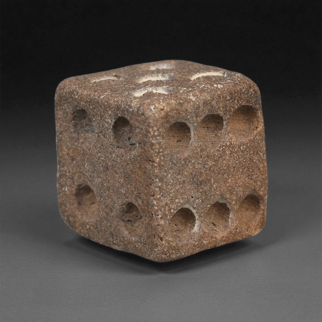 A Roman Bone Die, 1st-3rd Century CE, 78ZA: Carved from dense bone, the object is shaped as a small cube with slightly rounded edges. Each face bears a series of drilled circular pips arranged in standard numerical configurations. The surfaces 