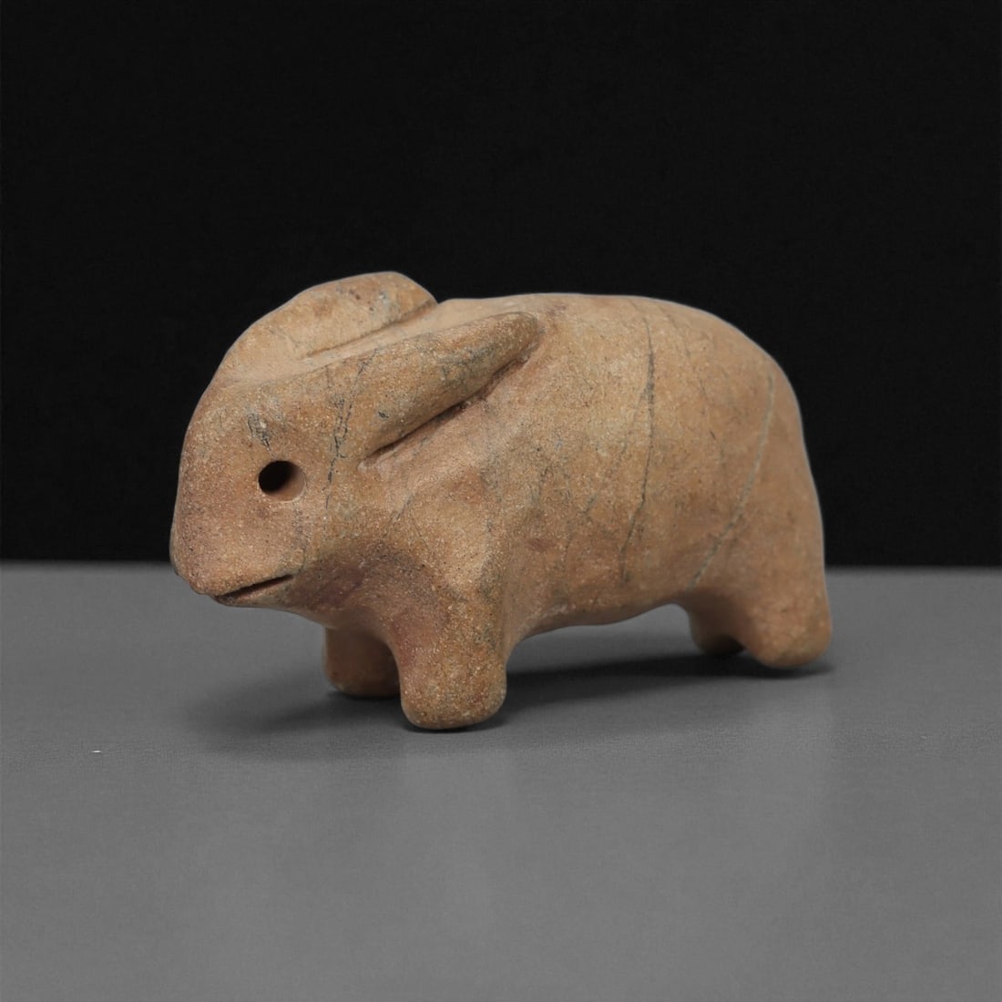 A Near Eastern Stone Zoomorphic Figurine, 3rd-2nd Millennium BCE, 70LB: Carved from a light brown stone with surface veining, the object depicts a compact quadruped with short legs and a rounded body. The head is rendered with a drilled circular eye and a small incised mo