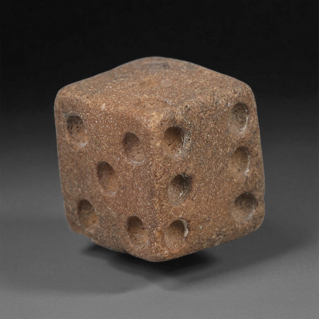 A Roman Bone Die, 1st-3rd Century CE, 33ZA: Carved from dense bone, the object is shaped as a small cube with slightly rounded edges. Each face bears a series of drilled circular pips arranged in standard numerical configurations. The surfaces 