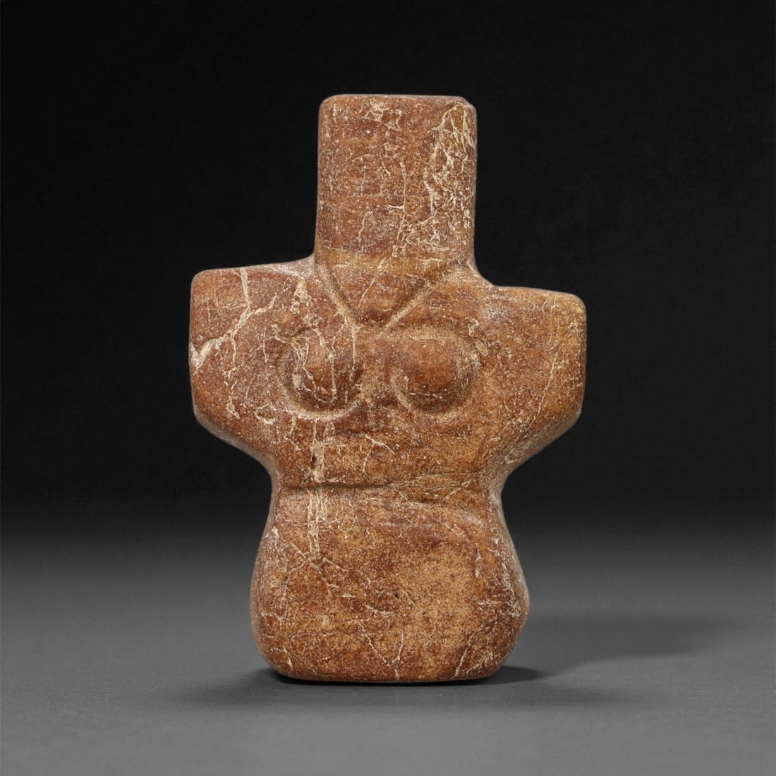 A Near Eastern Stone Anthropomorphic Idol, 3rd-2nd Millennium BCE, 58LA: Carved from mottled brown stone with light surface veining, the figure is shaped with a broad, cross-like upper body and a tapering lower section. The head is cylindrical and unarticulated, while the 