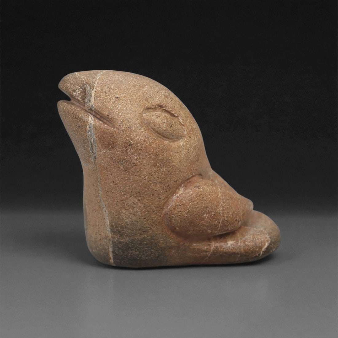 A Near Eastern Stone Bird Figurine, 3rd-2nd Millennium BCE, 79LB: Carved from a brown stone with lighter surface veining, the object depicts a stylized bird seated upright, the head tilted slightly upward. The beak is indicated by a shallow horizontal incision divid