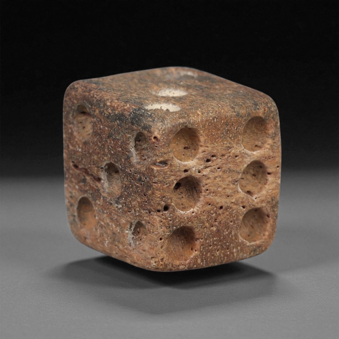 A Roman Bone Die, 1st-3rd Century CE, 13ZA: Carved from dense bone, the object is shaped as a small cube with slightly rounded edges. Each face bears a series of drilled circular pips arranged in standard numerical configurations. The surfaces 