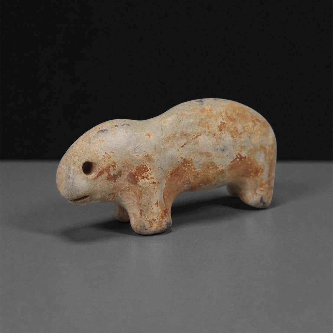A Near Eastern Stone Zoomorphic Figurine, 3rd-2nd Millennium BCE, 24LB: Carved from pale brown stone with scattered surface accretions, the figure is shaped as a compact quadruped with a rounded body and short legs. The head is modeled with a drilled circular eye, a small