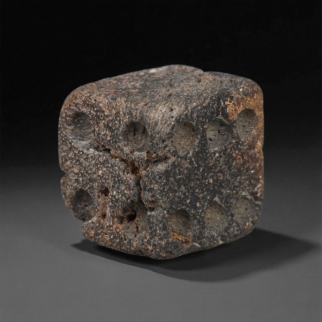 A Roman Bone Die, 1st-3rd Century CE, 83ZA: Carved from dense bone, the object is shaped as a small cube with slightly rounded edges. Each face bears a series of drilled circular pips arranged in standard numerical configurations. The surfaces 