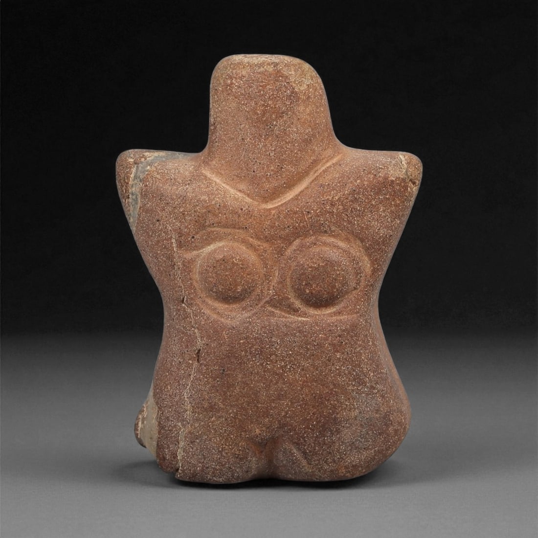 A Near Eastern Stone Female Idol, 4th-3rd Millennium BCE, 50LB: Carved from a reddish-brown stone with fine surface inclusions, the figure is modeled with a short neck above broad, slightly projecting shoulders. The breasts are rendered as two rounded discs with c