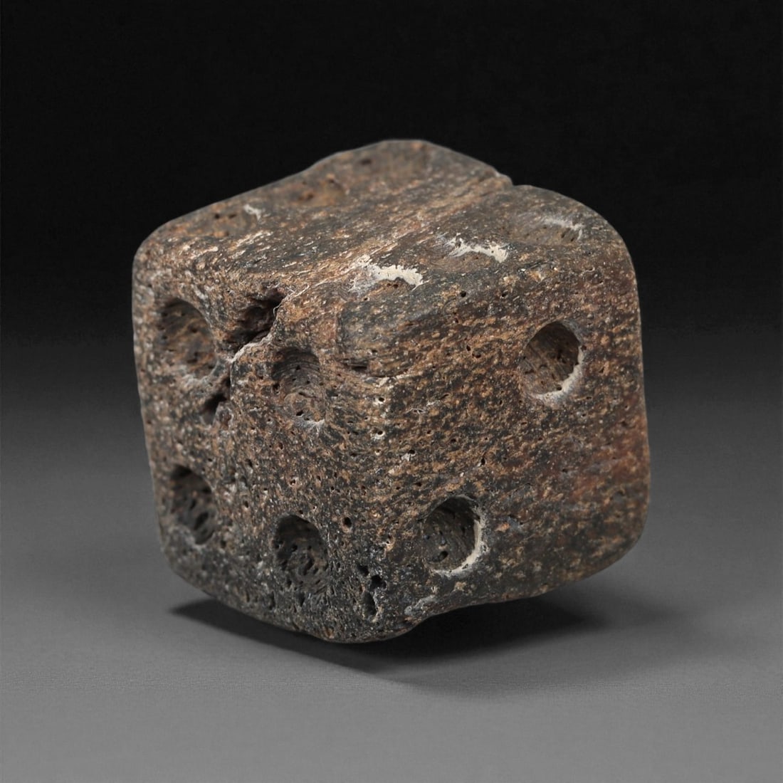A Roman Bone Die, 1st-3rd Century CE, 48ZA: Carved from dense bone, the object is shaped as a small cube with slightly rounded edges. Each face bears a series of drilled circular pips arranged in standard numerical configurations. The surfaces 