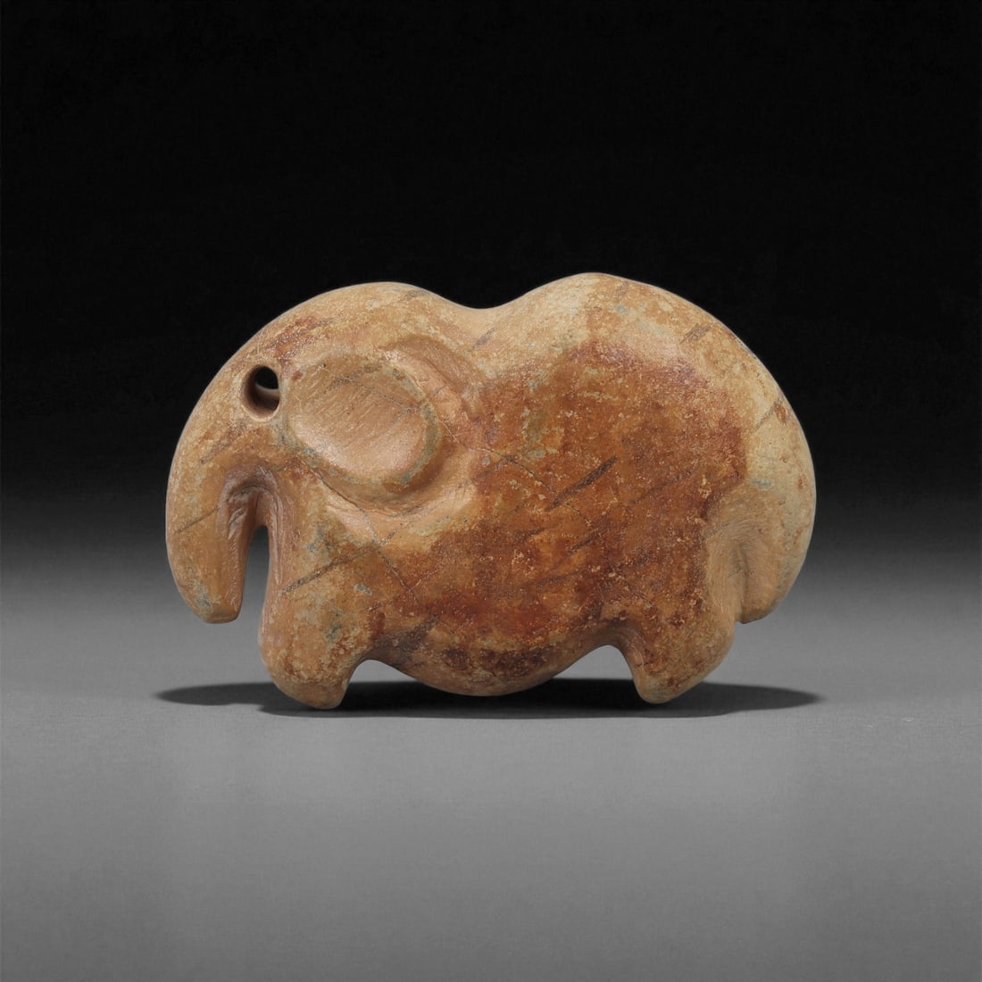 A Near Eastern Stone Elephant Figurine, 3rd-2nd Millennium BCE, 84LA: Carved from light brown stone with patches of surface accretion, the figure depicts an elephant in profile with a rounded body supported on four short legs. The head features a drilled circular eye, a