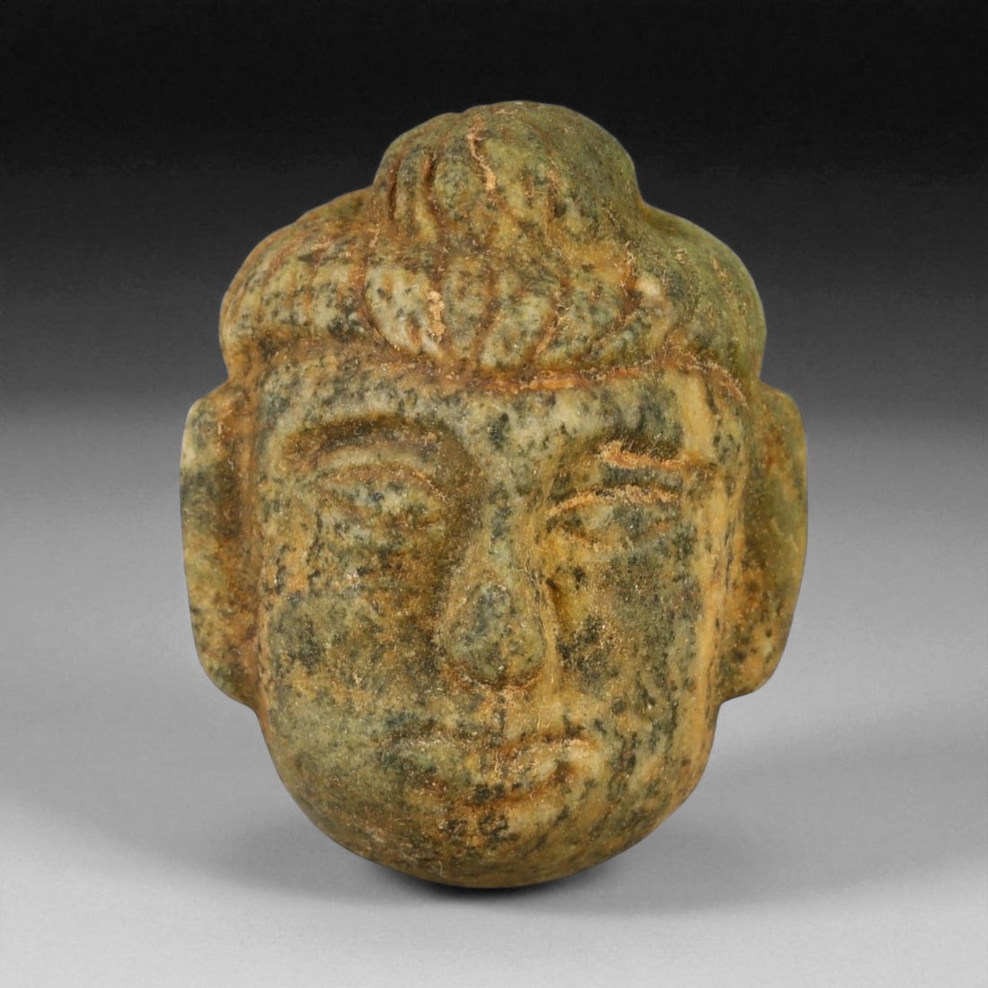 Ancient Gandharan Green Stone Head Amulet, c. 2nd-4th Century CE, 3.6cm, 18G: This delicately carved green stone head amulet originates from the ancient Gandhara region, c. 2nd-4th century CE, a time when Greco-Buddhist art flourished along the crossroads of South and Central A