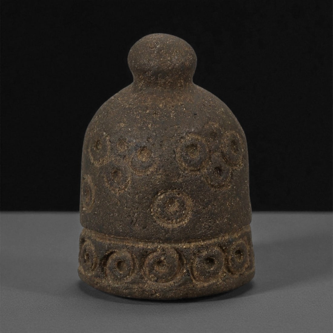 A Near Eastern Stone Weight, 2nd-1st Millennium BCE, 53LE: Carved from a dark brown stone with a fine granular texture, the weight is shaped as a domed cylinder surmounted by a rounded knob. The surface is decorated with incised concentric ring motifs arrange