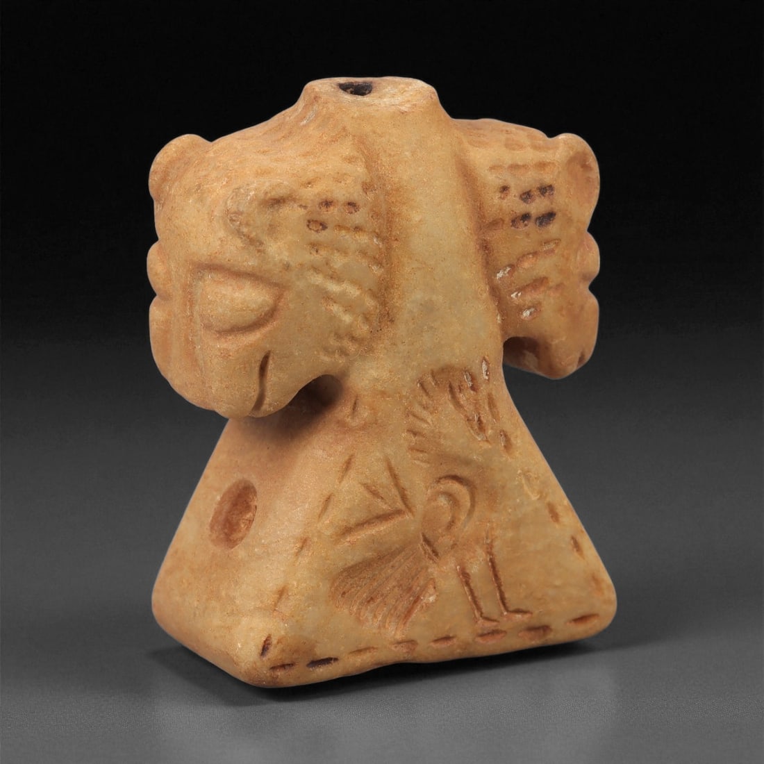 A Near Eastern Stone Kohl Vessel, 2nd-1st Millennium BCE, 74LE: Carved from a pale orange-beige stone with smooth surfaces, the vessel has a narrow cylindrical neck rising from a broad, triangular lower body. The upper section is modeled as a pair of opposed anima
