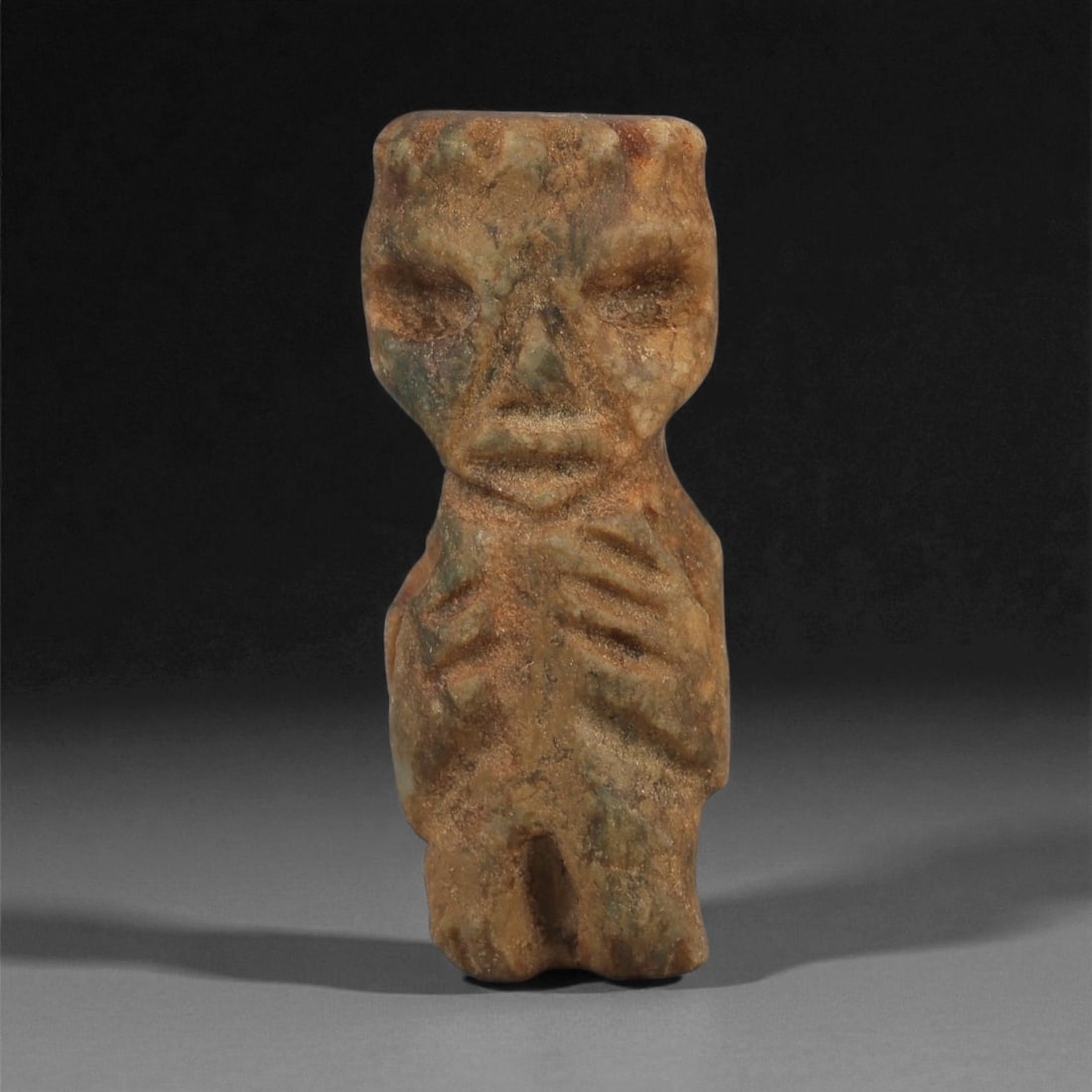A Taino Carved Stone Idol, Late Pre-Columbian Period, Circa 1000-1500 CE, 83LF: Carved from a mottled brown-green stone with minor surface pitting, the figure is rendered standing with the legs joined at the lower section and divided by a shallow vertical groove. The torso is mod