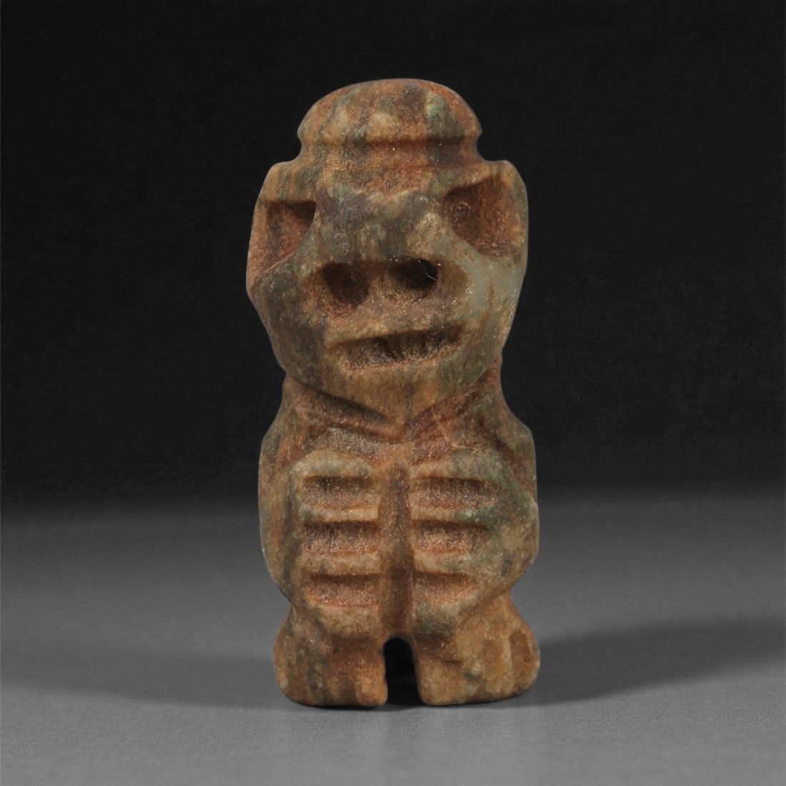 A Taino Carved Stone Idol, Late Pre-Columbian Period, Circa 1000-1500 CE, 85LF: Carved from a mottled brown-green stone with natural surface inclusions, the figure is rendered standing with legs separated by a deep central groove. The torso is shaped with rounded chest forms and 