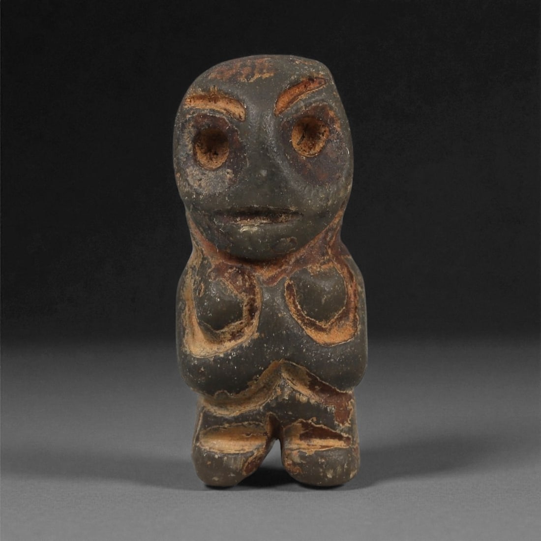 A Taino Carved Stone Idol, Late Pre-Columbian Period, Circa 1000-1500 CE, 94LF: Carved from a dark gray stone with reddish surface accretions, the figure is depicted standing with the legs partially separated by a shallow vertical groove. The torso bears a pair of rounded recesse