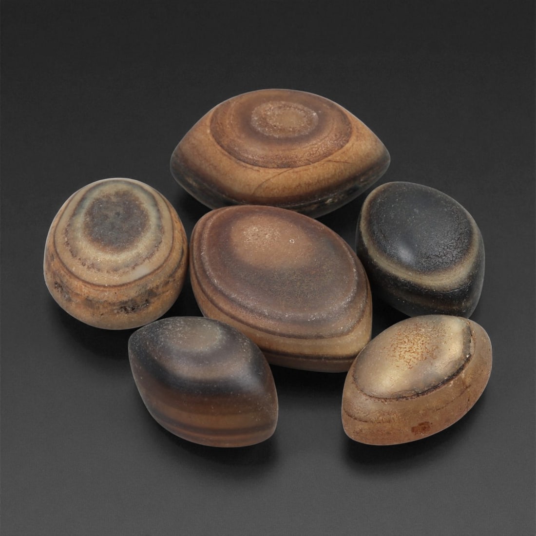 A Group of Tibetan Stone Luk Mik ("Goat Eye") Beads, 19th-Early 20th Century, 27LG: Carved from banded agate and chalcedony, the group comprises six domed, oval, and lenticular beads characterized by concentric circular banding that creates the "eye" motif associated with luk mik for