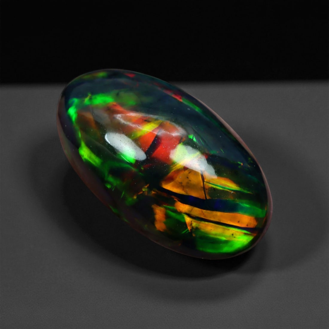 5.12 Carats Flame Pattern Black Opal Cabochon - Natural Ethiopian Stone, 46XE: This mesmerizing black opal features a kaleidoscopic flame pattern of glowing emerald, fiery red, and molten orange erupting beneath a deep, translucent surface. The color play appears layered and alm