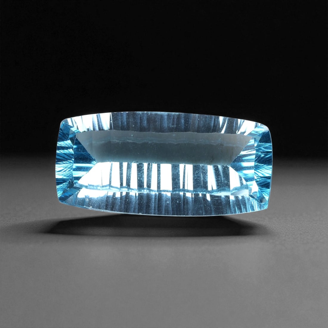 18.67 Carats Sky Blue Topaz Fancy Cut - Natural Brazilian Gemstone, 77XC: This elegant blue topaz gleams with a crystalline sky blue hue, precision-cut into an elongated cushion shape with a dramatic concave faceting pattern. The sculpted pavilion draws light inward and amp