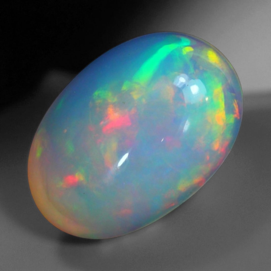 6.70 Carats Fiery Play-of-Color Welo Opal Oval Cabochon - Natural Ethiopian Stone, 29WE: This mesmerizing Welo opal radiates a luminous play-of-color that dances across its translucent body in vivid flashes of red, orange, green, and violet 17.1x11.9x7.5mm. The gem's opalescent base glows