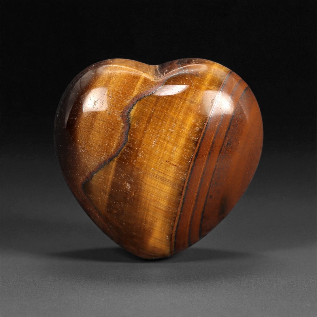 98.28 Carats Golden Brown Tiger's Eye Heart - Natural South African Carving, 88XC: This richly polished tiger's eye heart reveals bold waves of golden brown chatoyancy, shifting fluidly with the light like satin ribbon. Its silky luster and natural bands of amber, caramel, and deep 